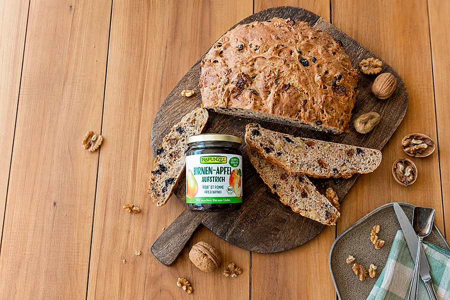Fruchtiger Brotaufstrich mit Früchtebrot. Ein Glas Apfel-Birnen-Kraut steht auf einem Brettchen neben geschnittenem Früchtebrot zum Bestreichen.