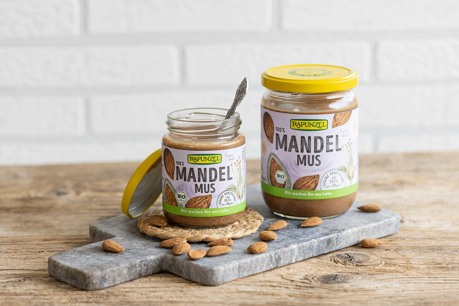 Rapunzel Mandelmus braun – 100 % Mandeln, Bio-Qualität in zwei Größen. Zwei Gläser Rapunzel Mandelmus braun in unterschiedlichen Größen auf einem Marmorbrett – cremiges Bio-Nussmus aus 100 % Mandeln.