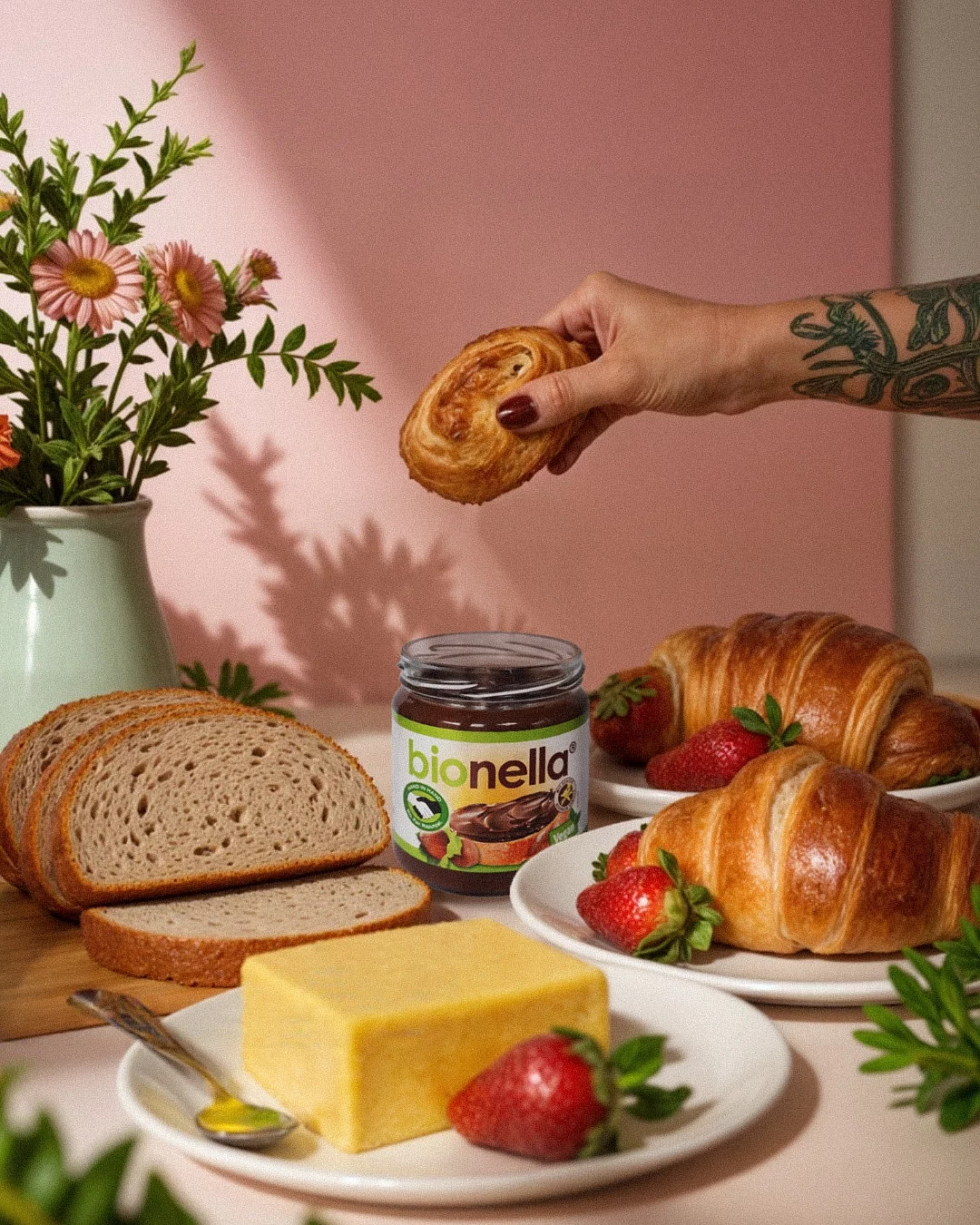 bionella Glas auf fancy Frühstückstisch bionella Glas auf Frühstückstisch mit Butter und Brötschen mit rosa Hintergrund