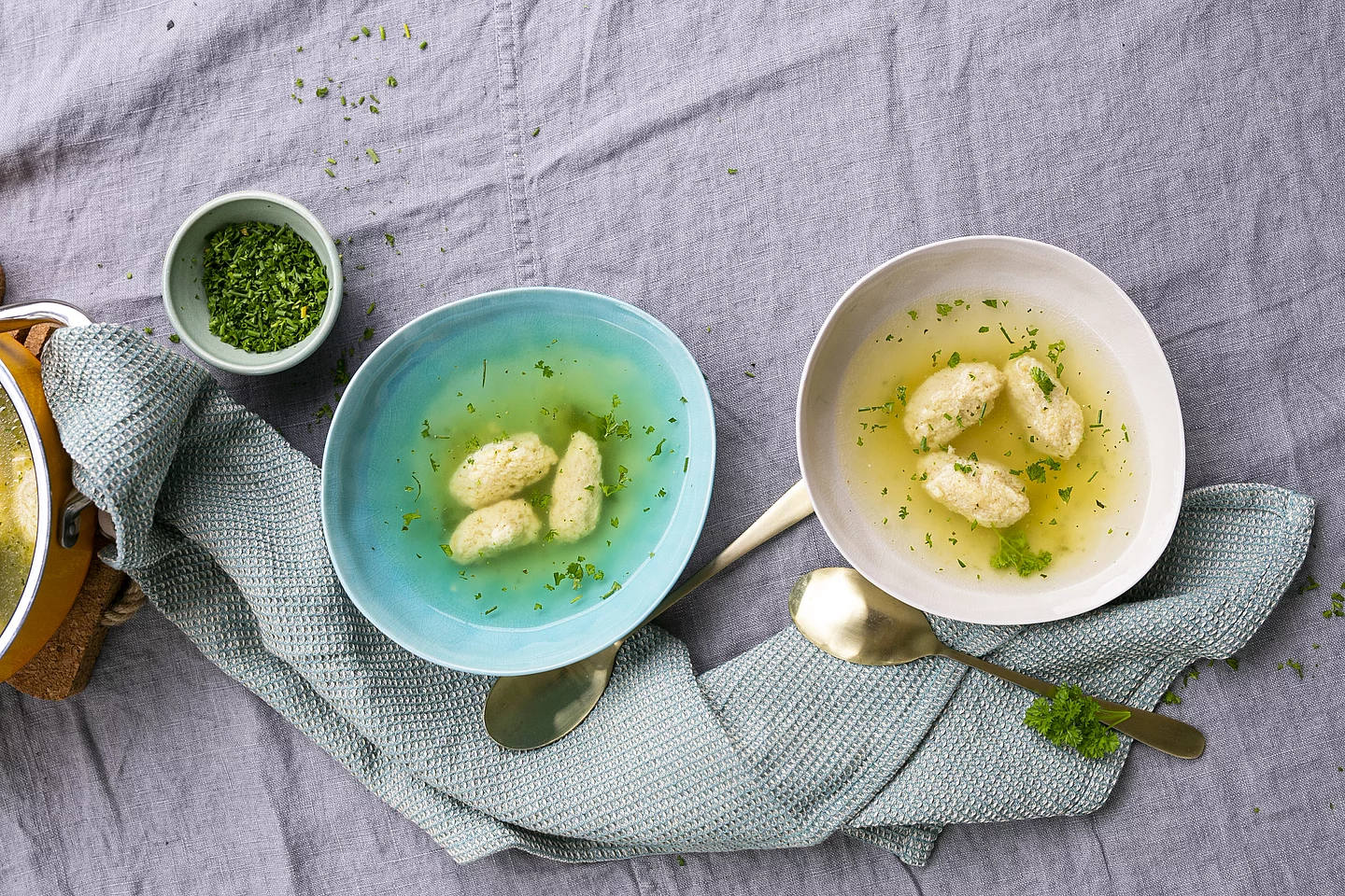 Griesnockerlsuppe mit Klarer Suppe mit Bio-Hefe. Zwei Teller mit Griesnockerlsuppe mit Klarer Suppe auf einem Tuch.