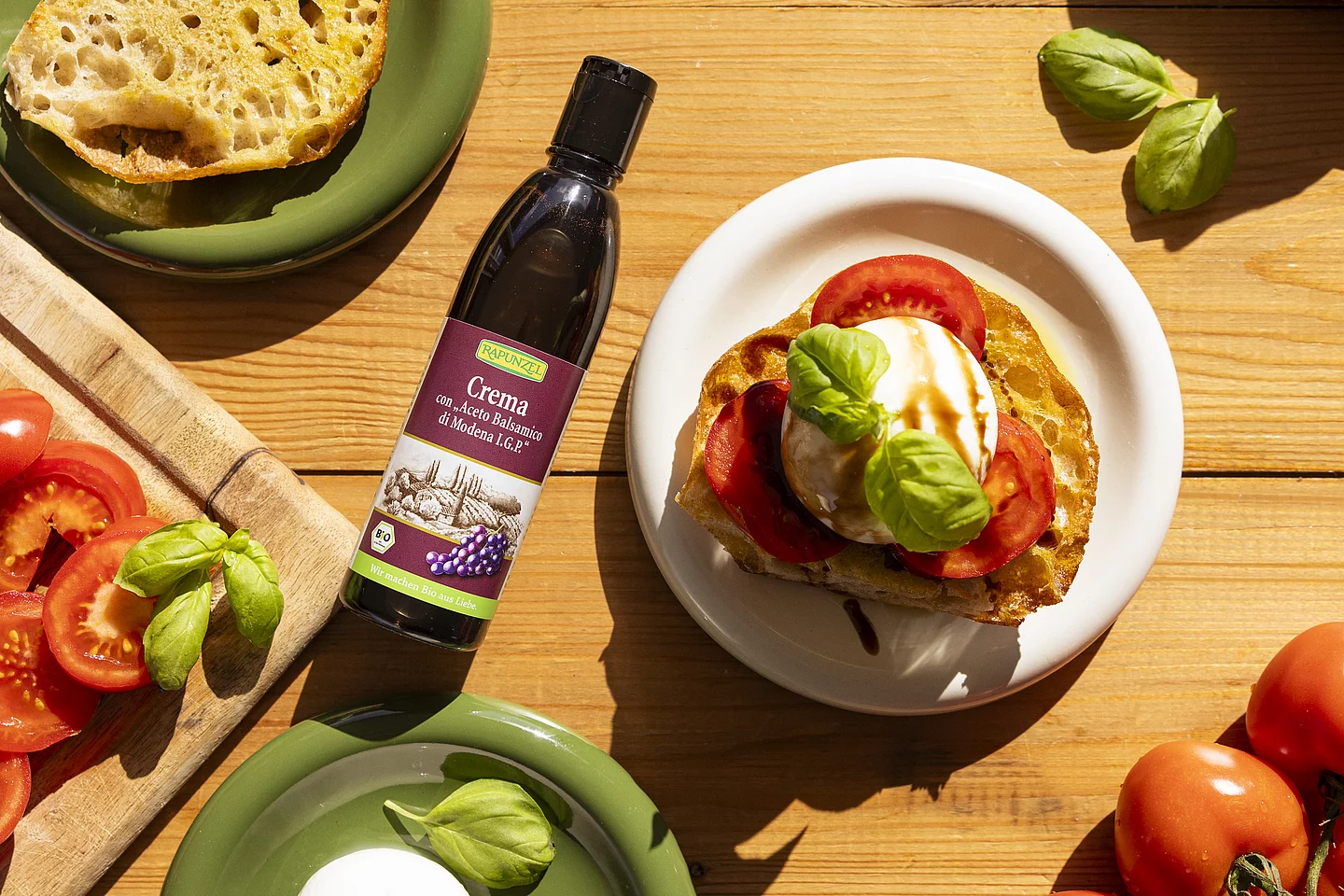 Die Rapunzel Crema con 'Aceto Balsamico di Modena I.G.P.' verfeinert Salate und Früchte sowie Desserts. Baguette mit Burrata und Tomate neben einer Flasche Rapunzel Crema con 'Aceto Balsamico di Modena I.G.P.'