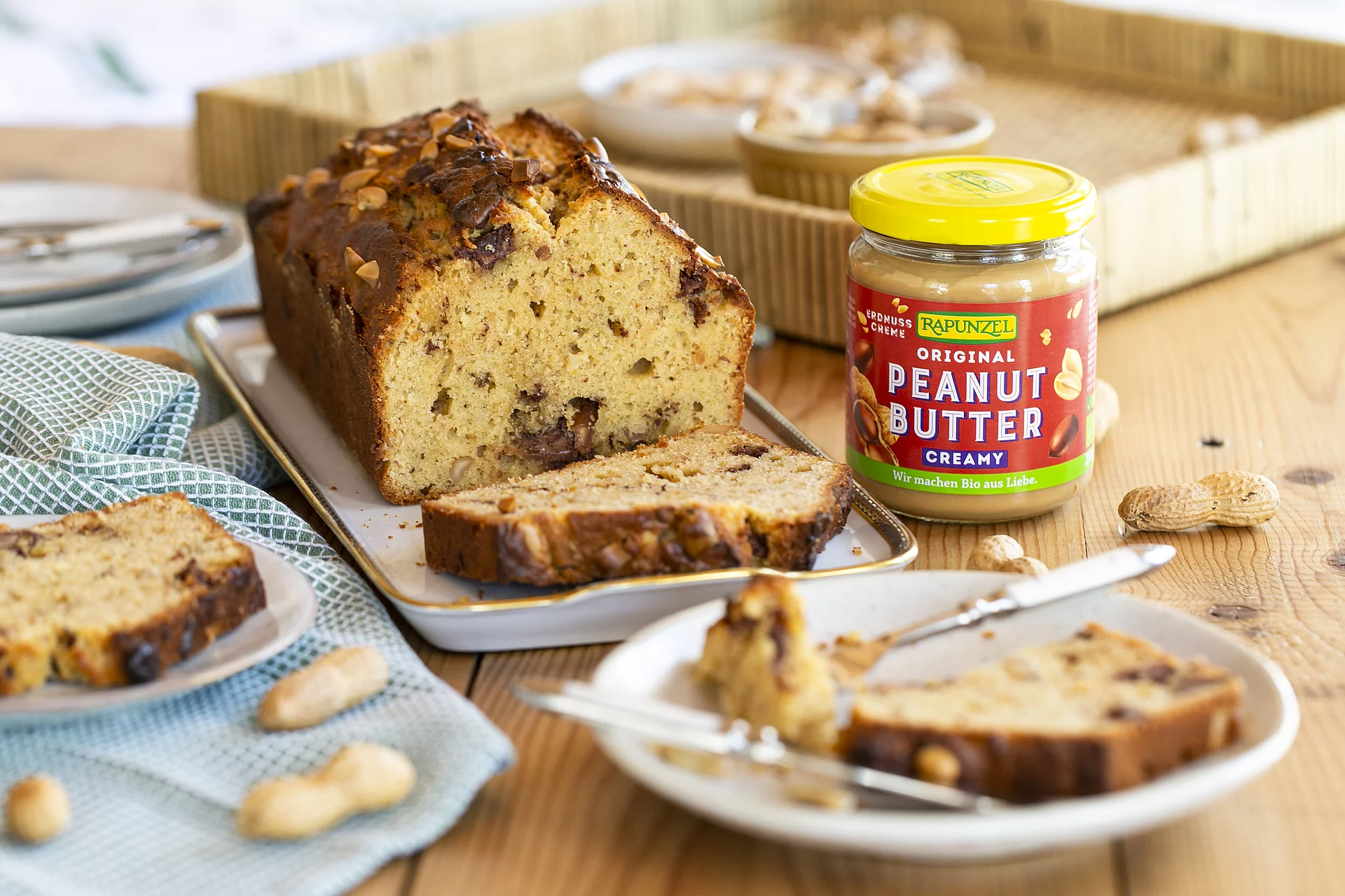 Peanutbutter als Zutat für kreative Genussmomente. Ein Glas Peanutbutter steht auf einem Holztisch neben einem Kuchen. Einige Erdnüsse liegen daneben und ergänzen die natürliche Bildszene.