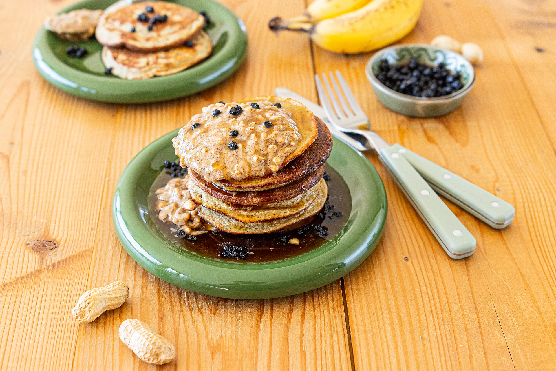 Glutenfreie Pancakes mit Erdmandeln. Mehrere Pancakes übereinandergeschichtet auf grünem Teller auf einem Tisch.