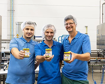 Drei Mitarbeitende halten ein Glas Mandelmus.