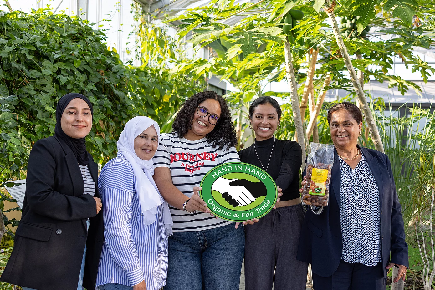 Gruppenfoto im Tropenhaus von Rapunzel mit CCF-Gründerin Samia Chibani. Mit im Bild sind das HAND IN HAND-Logo und die Datteln, die von Rapunzel verkauft werden.