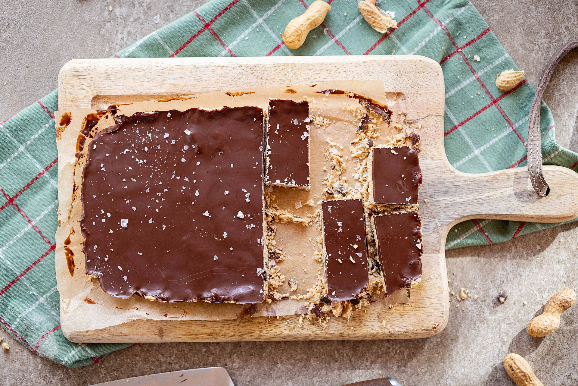 Erdnuss-Protein-Riegel. Großes Stück Erdnuss-Protein-Riegel auf einem Brett, einzelne Riegel sind schon abgeschnitten.