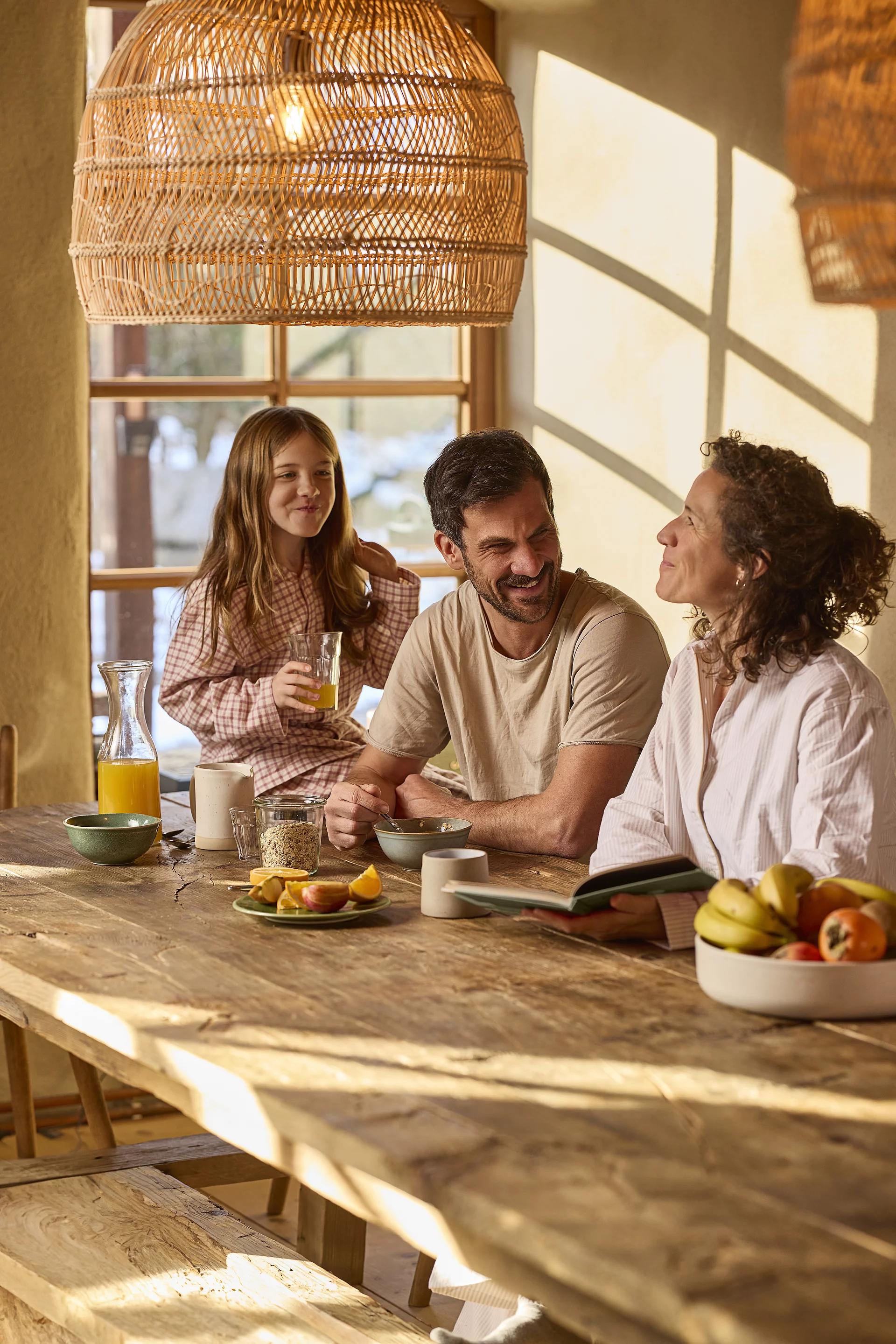 Eine Familie genießt gemeinsam ein Frühstück mit Müsli in einer ländlichen, bauernhofähnlichen Umgebung. Mutter, Vater und Kind sitzen zusammen am Frühstückstisch.