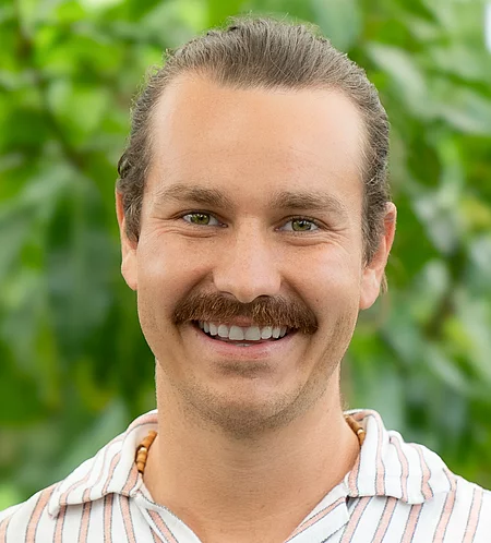 Manuel Kämmerle Rapunzel Mitarbeiter steht vor blühender Pflanze.